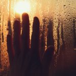 Hand touches a misty window with sunlight.
