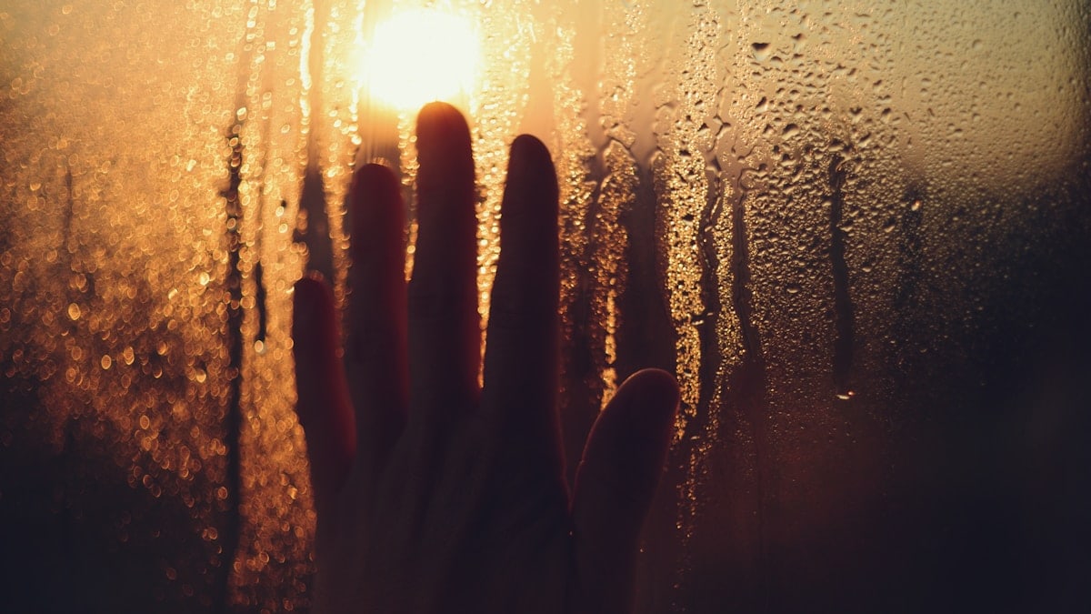 Hand touches a misty window with sunlight.