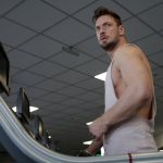 Low angle of muscular adult male athlete in sportswear during training on running machine in modern spacious fitness center while looking away